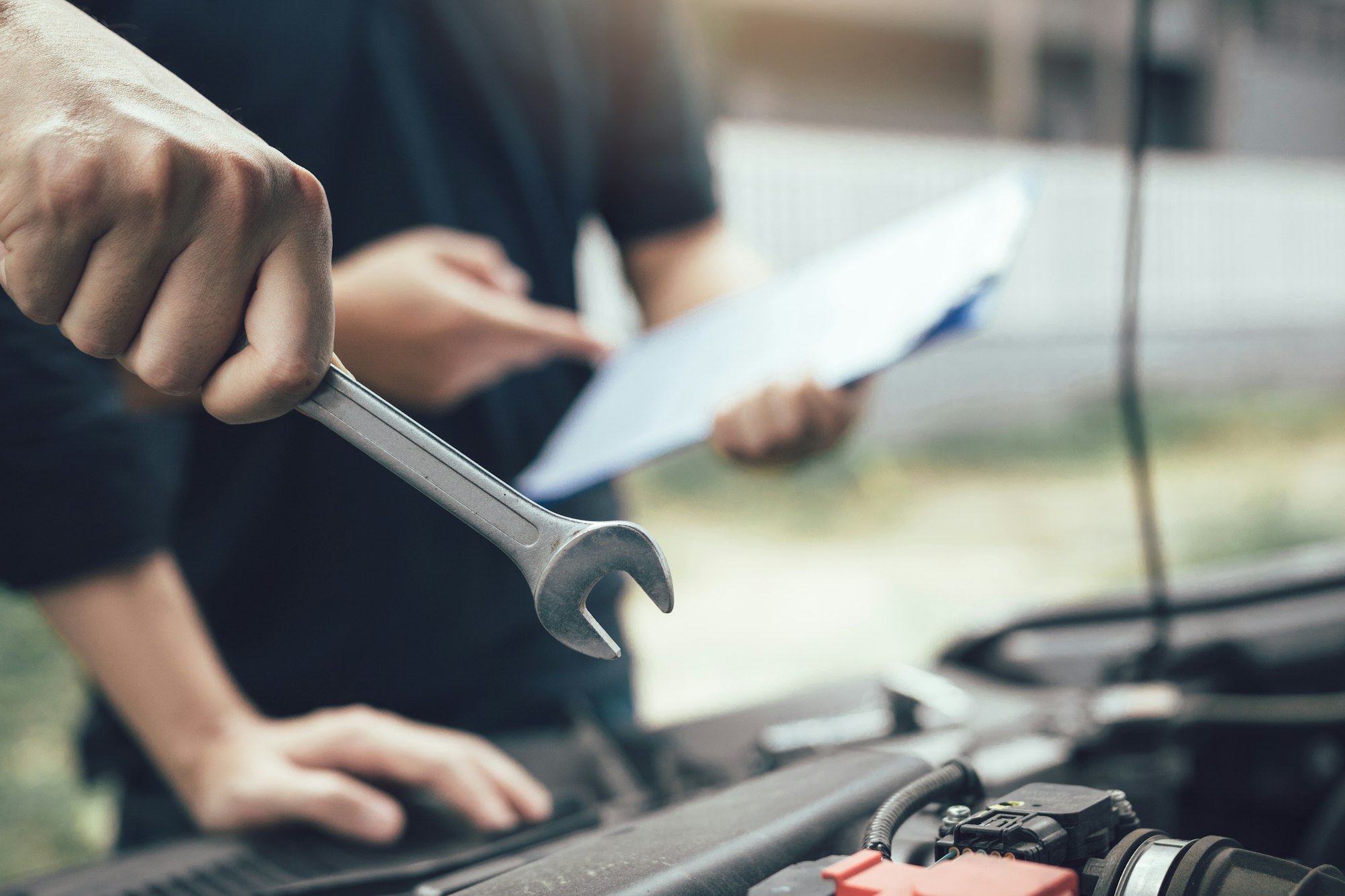 Car mechanic is holding a wrench ready to check the engine and maintain it with the assistant.